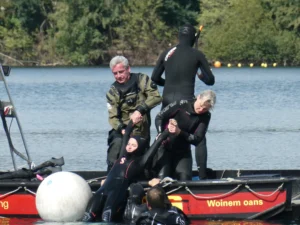 Taucherin wird an beiden Armen aus dem Wasser ins Boot gezogen.